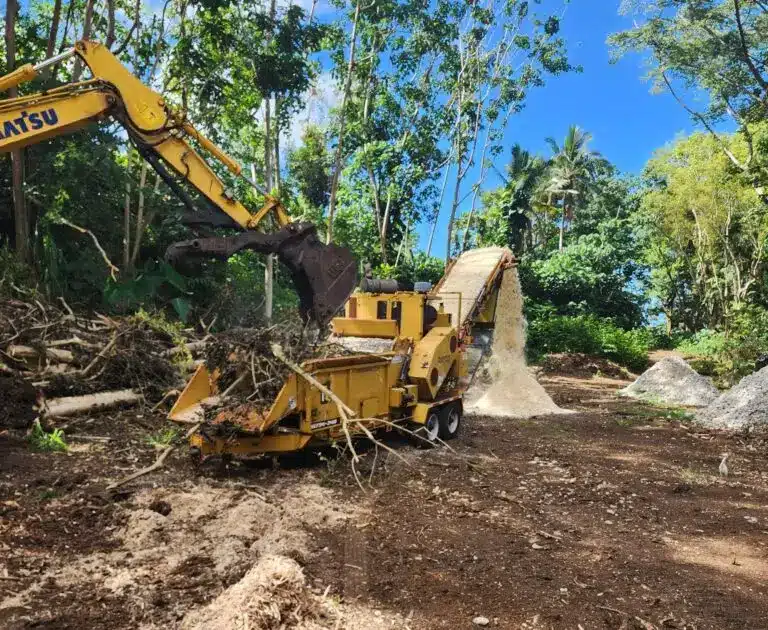 Excavator feeding a grinder during land clearing on Oahu